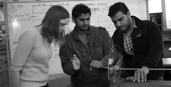 Three students looking at a device in a classroom.