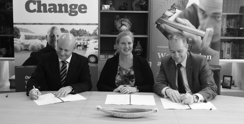 Three officials at a table signing papers